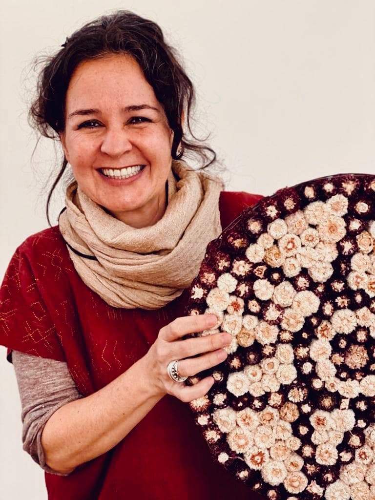 Genoveva De La Peña sonríe sosteniendo un arreglo circular de flores secas