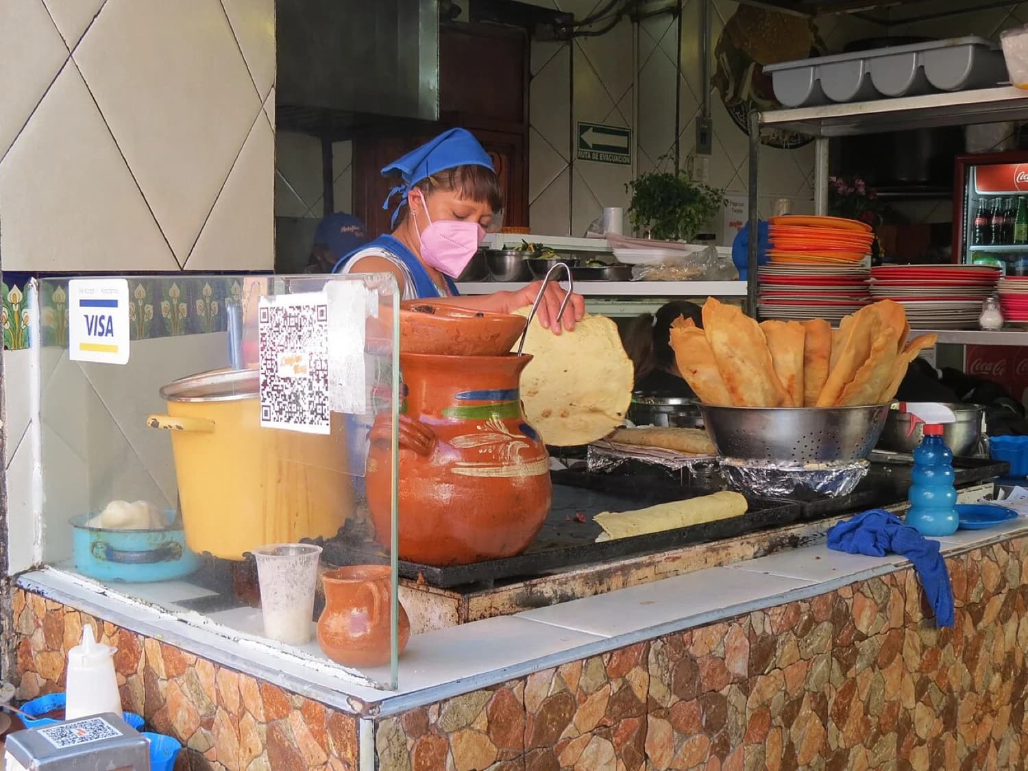 Mujer dando vuelta a las tortillas sobre un comal en la vía pública